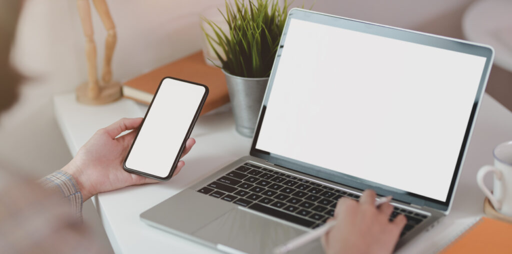 Young businesswoman typing on laptop while holding smartphone